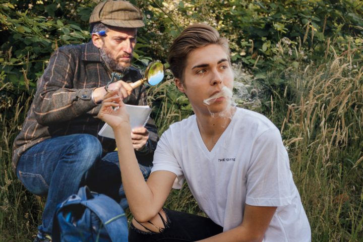 A guy smoking a joint while a man with a magnifying glass looks at him.