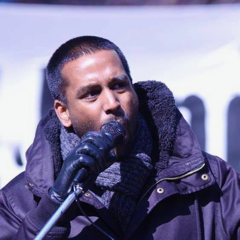 A picture of Krisna Saravanamuttu speaking into a microphone at a solidarity rally with the Kitchenuhmaykoosib Inninuwug (KI) nation to stop mining on their traditional burial grounds.