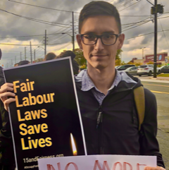 A photo of Erin Sobat outside holding a sign that says “Fair Labour Laws Save Lives – 15andfairness.org”.