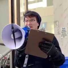 A photo of Adam Lee co-emceeing an outdoor Toronto Prisoners’ Rights Project rally, speaking into a megaphone and holding a clipboard.
